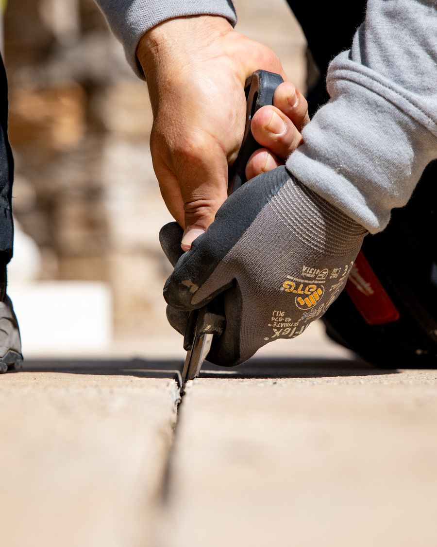 Pool Mastic Pros technician cutting failed mastic out of a pool deck expansion joint